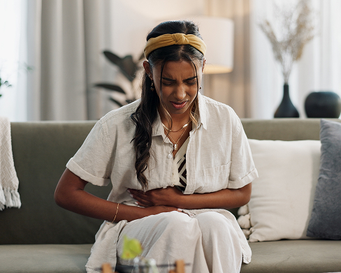 woman sitting on couch holding her abdomen in discomfort 